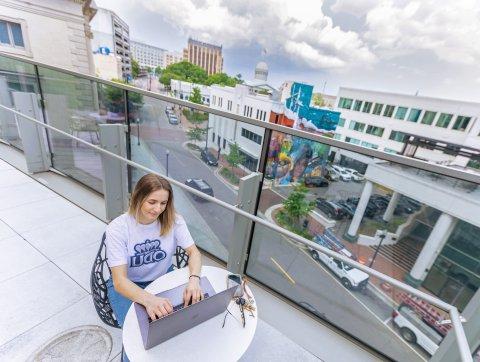 a female student with blond hair and a white odu t-shirt is sitting on a rooftop in a downtown area studying